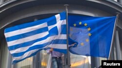 Belgium -- A man adjusts a Greek (L) and a EU flags outside the Greek embassy in Brussels, February 19, 2015