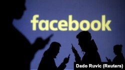 Silhouettes of mobile users are seen next to a screen projection of Facebook 